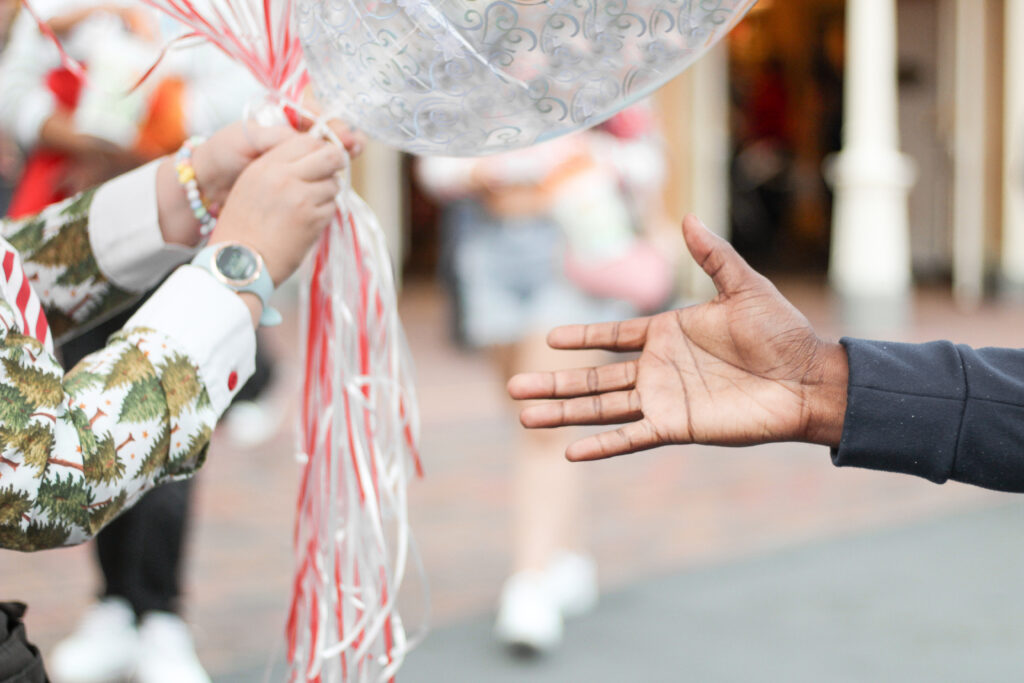 guest hand held out to a balloon vendor holding a rack of Christmas balloons along Main Street, U.S.A.