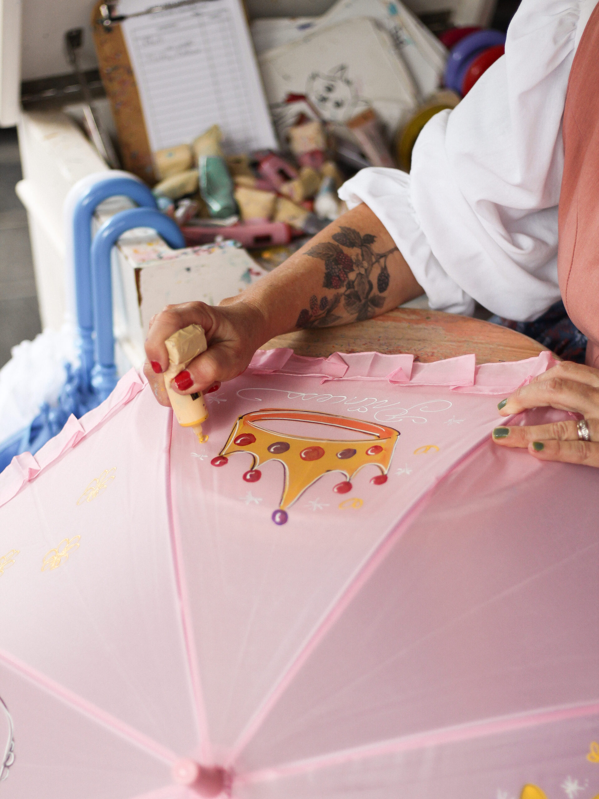 Magic Kingdom parasol artist Virginia painting a tiara on a pink parasol